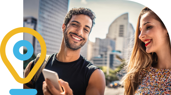 Um homem sorrindo e mostrando o celular pra uma mulher, ambos brasileiros, no fundo uma cidade.